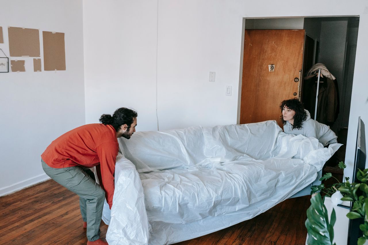 who-we-are A couple collaboratively lifting a couch while moving into a new apartment.